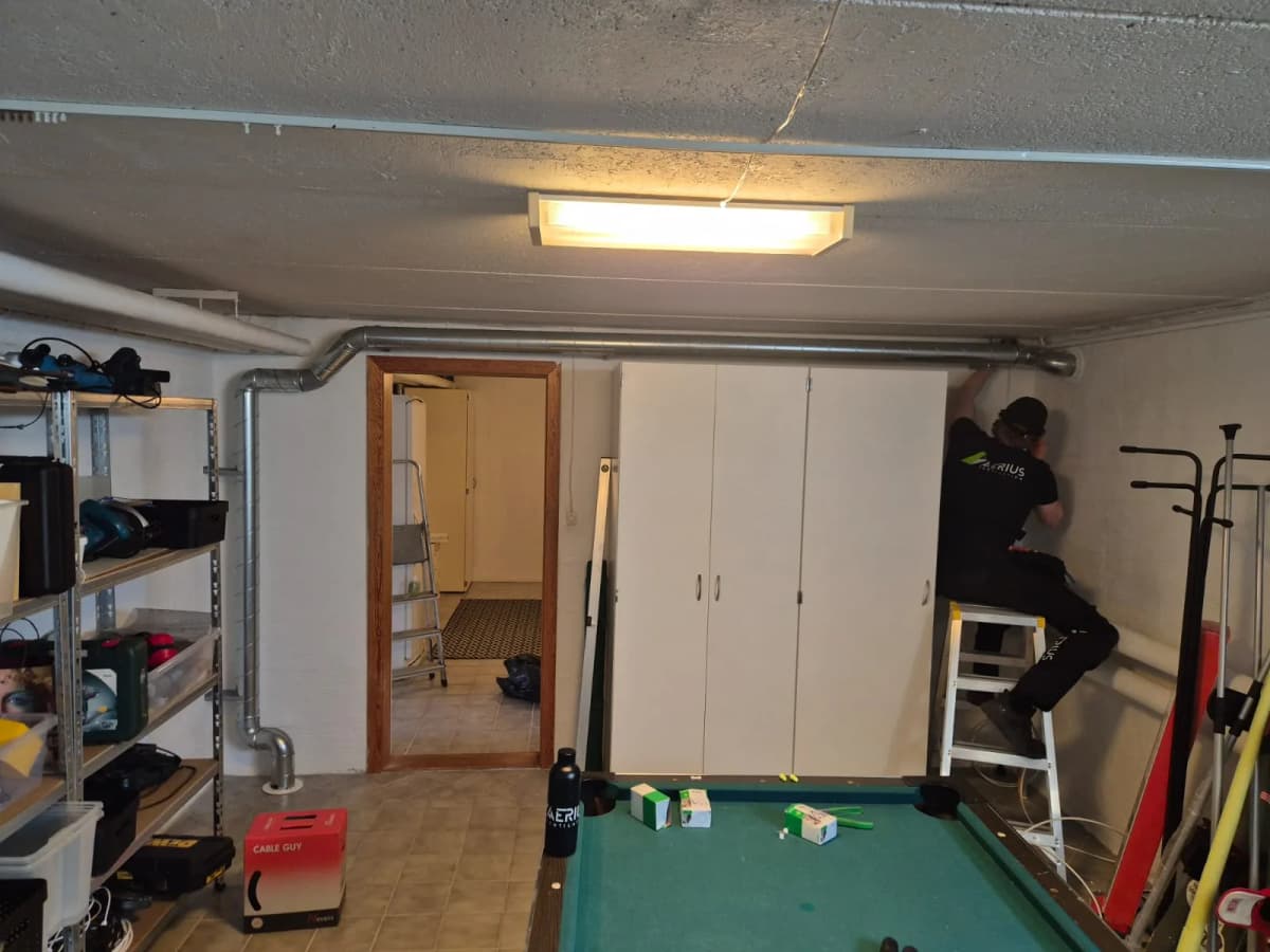 Tekniker på stege monterar kanal längs källartaket i ett hobbyrum under installation av radonsug